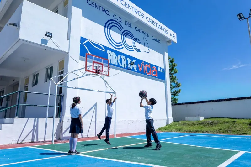 Alumnos de primaria juegan en la cancha de basquetbol junto al edificio